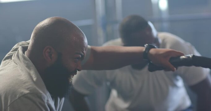 African American men training, coach leaning in encouraging, trainee pulling battle rope powerfully