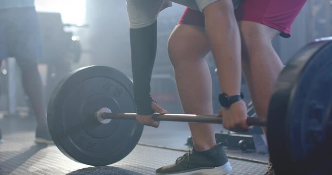 African American men coach touching bar lifter red shorts bracing lifting barbell for safety at gym
