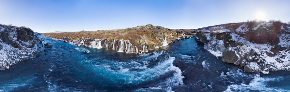 Aerial view of icy waters cascade down from volcanic rock formations at Hraunfossar waterfall, with Hvita river and snow-dusted landscape, in 360 degrees panorama, Vesturland, Iceland.