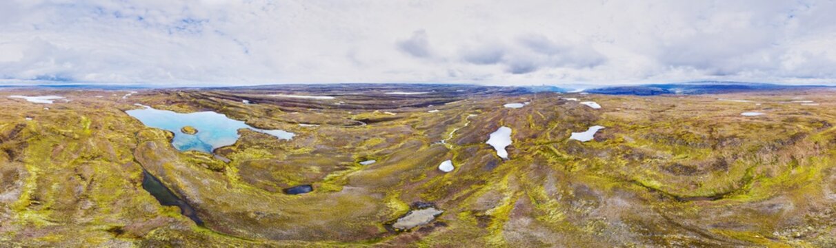 Aerial view of a vibrant landscape dotted with turquoise pools and stark white snow patches under a vast, cloudy sky, in 360 degrees panorama, Kollabudaheidi, Westfjords, Iceland.
