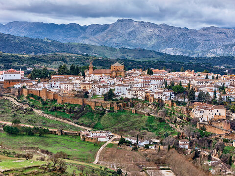 Aerial view of the ancient city walls embracing the whitewashed buildings, under a dramatic sky, with the distant mountains completing the scene, Ronda, Andalusia, Spain.