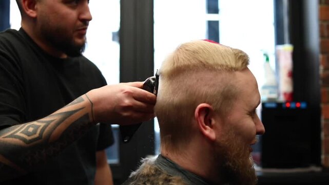Barber cutting a man&rsquo;s hair with clippers in a barbershop. Side profile of a male client with short haircut and beard, professional grooming service in a salon.
