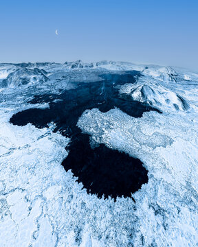 Aerial view of stark dark lava flows cutting through a serene snow-covered landscape under a pale sky, Reykjav&Atilde;&shy;k, Reykjav&Atilde;&shy;kurborg, Iceland.
