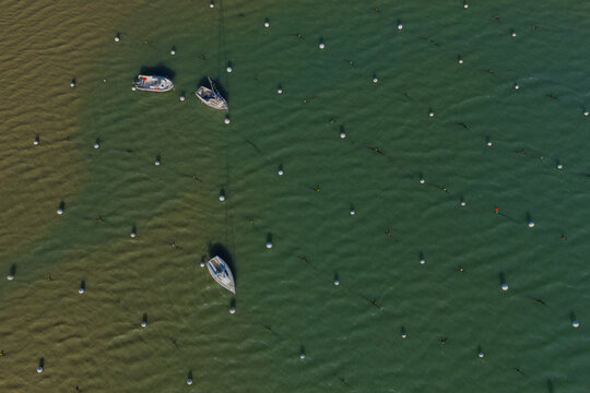 Aerial view of boats floating on the water with white spherical markers, creating a geometric pattern against the water, Saint-Cast-le-Guildo, Brittany, France.