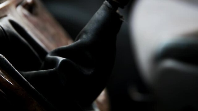 Close-up perspective of manual gear shifter inside car cabin, featuring dark leather boot and worn wooden knob. Controls for vehicle transmission, highlighting aged materials and functional design of 
