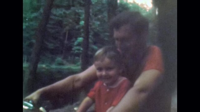 Happy young father with small son on motorcycle in nature. Strong confident parent enjoying summer with child outdoor. Family bonding, active lifestyle. Old film. Archival retro 1970s. Vintage archive