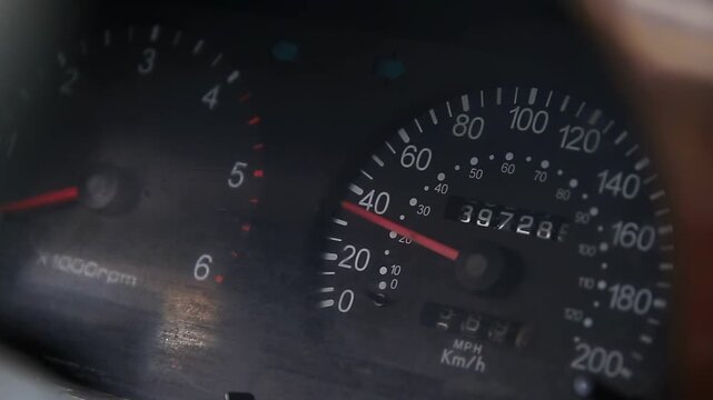 Close-up perspective of vehicle dashboard instruments. Speedometer needle fluctuates around 30-40 mph, odometer displays 39728 total mileage. Tachometer shows engine rpm. Indicators active.