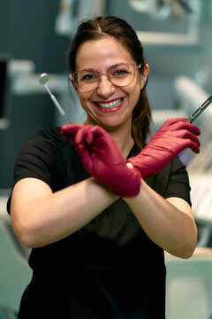 Friendly Female Dentist With Pink Gloves Demonstrating Dental Tools In Modern Clinic, Smiling, Caring, Professional