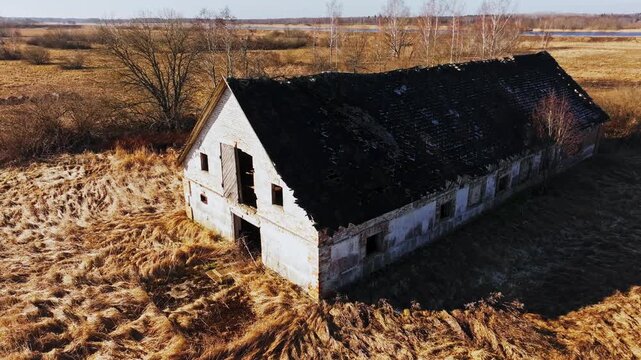 Cinematic aerial of decaying Soviet farm surrounded by golden dry spring field