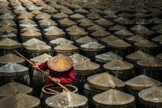 View of a craftsman stirring in a vast sea of dark, weathered vats of soy sauce / fish sauce under a soft light, all topped with conical lids in Xiapu, Fujian, China.