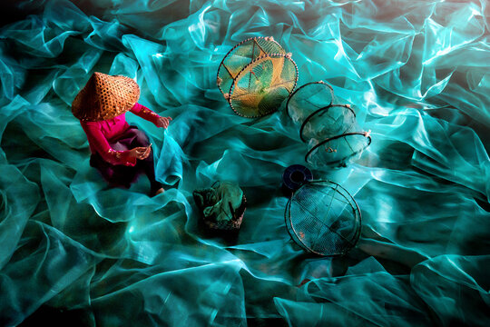 View of a person wearing a conical hat next to fishing equipment, mending turquoise coloured fishing net, all bathed in a soft, ethereal blue light, Xiapu, Fujian, China.