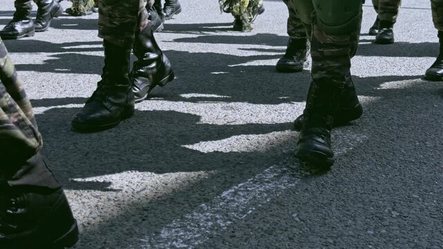 Low angle detail shot of army boots marching in sync on an asphalt road, representing military discipline and power