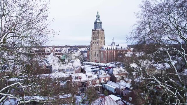Picturesque winter wonderland medieval Hanseatic Dutch tower town Zutphen in the Netherlands covered in snow aerial approach through winter barren trees