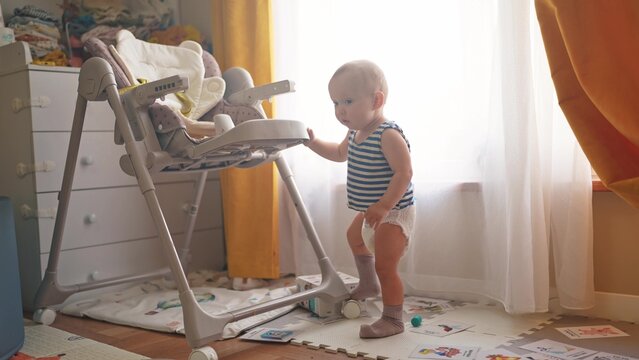a little boy stands near a chair and looks at the camera. happy family childhood dream concept. little son in diapers stands and looks away close-up window in lifestyle the background