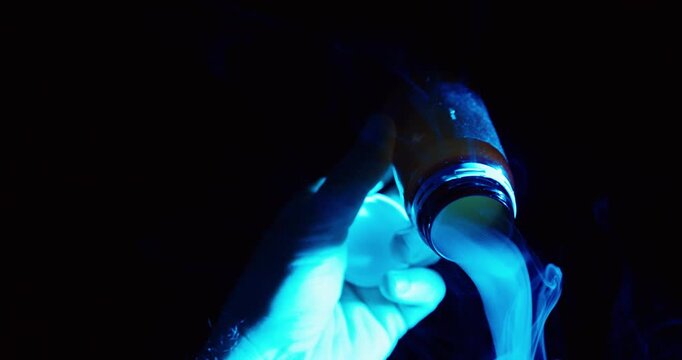 Dark cinematic close-up of a gloved hand holding an open medication bottle with smoke emerging, symbolizing drug abuse, addiction, substance dependency, and pharmaceutical misuse in a dramatic blue li