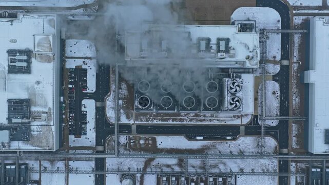 Modern industrial data center with spinning cooling fans emitting water vapor. Top down aerial view of the building surrounded by snow