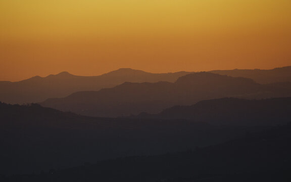 View of fiery sunset paints the sky in vibrant orange hues over the silhouette of rolling mountains creating a tranquil and picturesque landscape, Cesaro, Sicily, Italy.