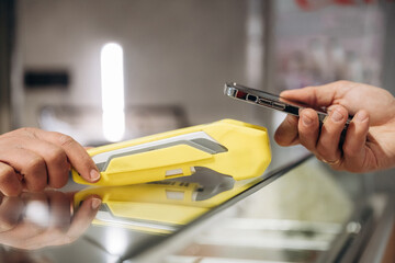 Obraz premium Two hands exchanging a yellow portable power bank and a smartphone over a glass counter in a modern retail store with bright lighting and minimalistic design