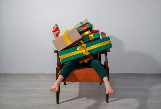 Boy sitting on chair indoors covered in colorful wrapped gifts