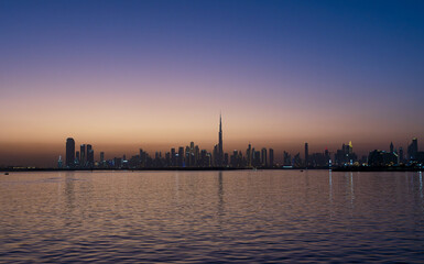 Fototapeta premium Mesmerizing Dubai skyline at dusk: Burj Khalifa silhouetted against a gradient sunset sky, city lights reflecting on calm waters.