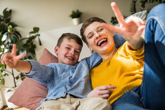 Happy woman and boy smiling and making victory gesture at home