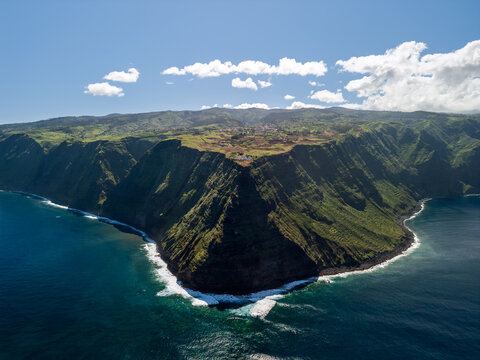 Drone panorama of Ponta do Pargo plateau Madeira Portugal, elevated aerial view highlights broad green tableland ending in sheer ocean cliffs with scattered rural buildings above Atlantic waters