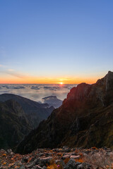 Fototapeta premium Sunrise above cloud sea and rugged peaks at Pico do Arieiro Madeira Portugal, warm light reveals volcanic ridges and deep valleys seen from mountain viewpoint at dawn