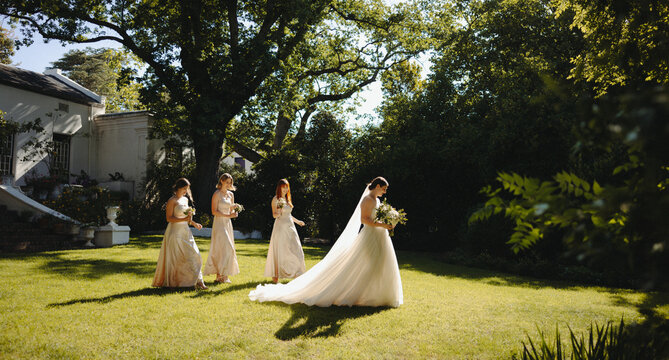 Bride and bridesmaids walking in sunlight at a garden wedding ceremony