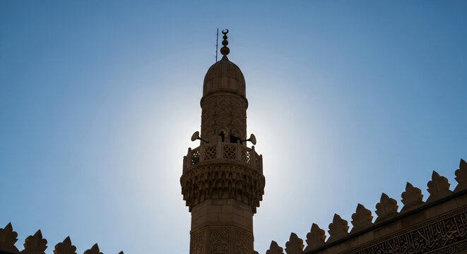 Backlit Stone Minaret Silhouette Against a Bright Blue Sky, Featuring Traditional Islamic Architecture and Crescent Symbol