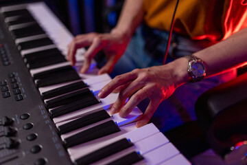 Hands playing digital piano keyboard. Musician creating music in home studio, Arts and Entertainment concept. Close-up of female hands on piano keys with moody blue and red professional lighting. © Graphicroyalty