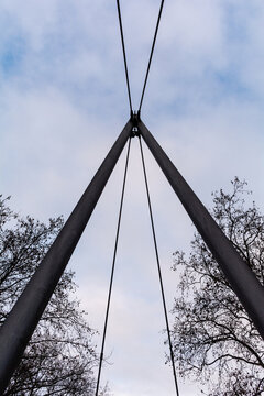View of steel bridge cables converging against a backdrop of a cloudy sky, framed by bare tree branches in the winter air, Nuremberg, Bavaria, Germany.