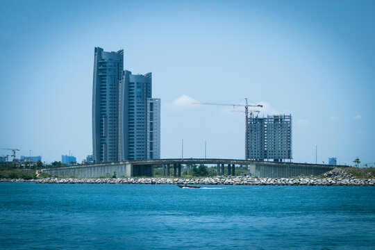 View of towering skyscrapers rise against the clear skyline, connected by a bridge over the serene water, contrasting modern architecture with natural beauty, Lagos, Lagos, Nigeria.