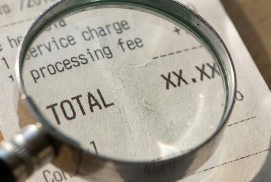 Close-up view of a receipt under a magnifying glass highlighting the total amount, with service charge and processing fee details visible on the paper