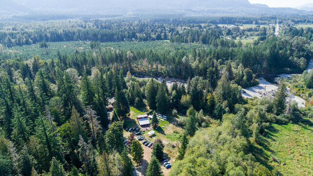 Aerial view of a rustic building nestled amidst dense forest, with vehicles parked nearby, framed by verdant trees and a winding river, Swede Heaven, Washington, United States.