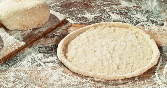 Super slow motion, 1000 fps of falling flour dusting freshly kneaded pizza dough on wooden table. Cinematic baking concept, preparation of homemade pizza and yeast dough.