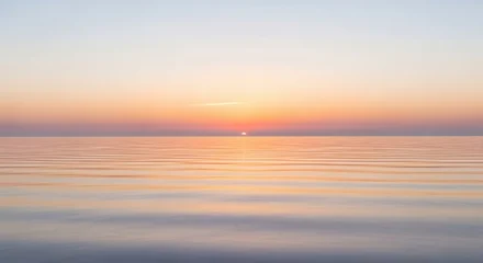 Fotobehang Zonsondergang Strand Serene seascape at dawn with smooth water and subtle wave patterns. Warm sunrise colors blend into a clear sky.  © Kak Budy