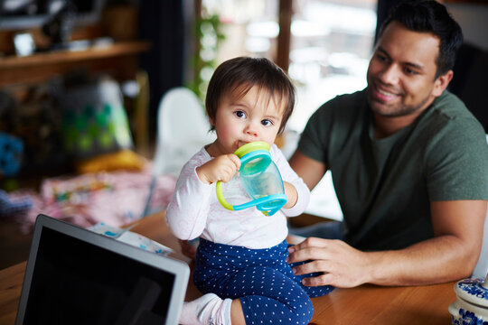 Portrait of baby girl sitting on table drinking water at home with father in background