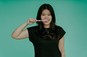Fototapeta premium Portrait of a smiling asian woman holding toothbrush isolated on green background. Smiling woman with healthy beautiful teeth holding a toothbrush. Dental health background.