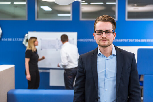 Businessman standing in conference room, while colleagues working with flipchart in background