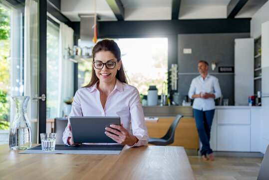 Smiling woman at home using a tablet at table with man in background