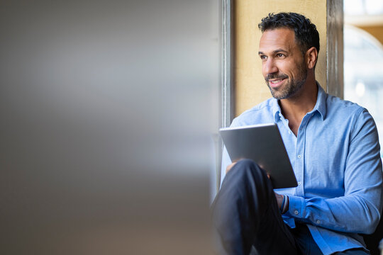 Smiling businessman sitting at the window using tablet