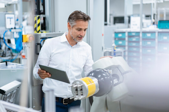 Businessman with tablet at assembly robot in a factory