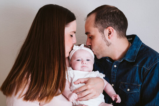 Parents kissing baby girl against wall at home
