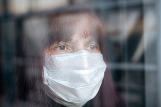 Portrait of senior women wearing a mask at home, looking out of the window