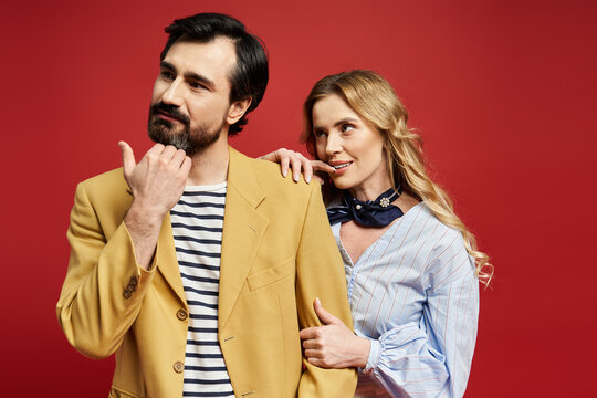 Stylish couple sharing a playful moment against a vibrant red background, radiating love and joy