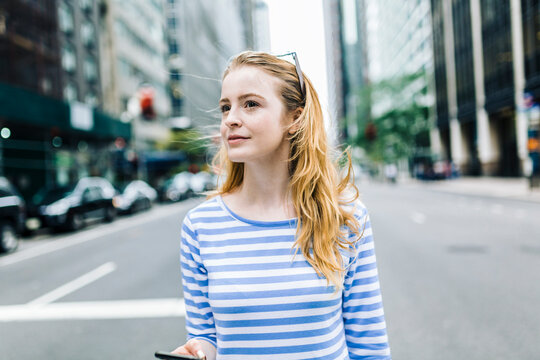 USA, New York, Manhattan, Young woman walking in the street, holding mobile phone