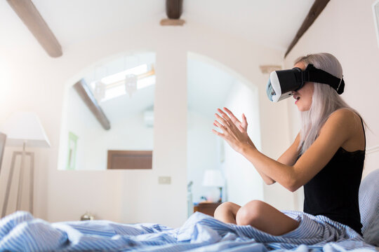 Amazed young woman sitting in bed wearing VR glasses