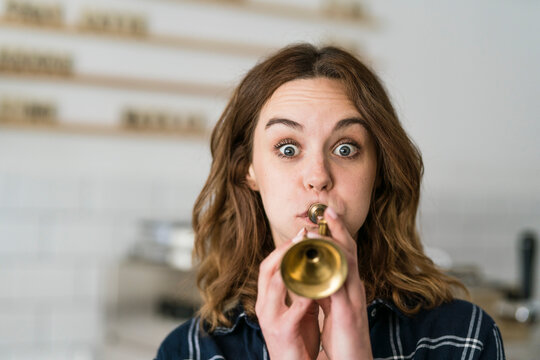 Young woman blowing toy trumpet in her coffee shop