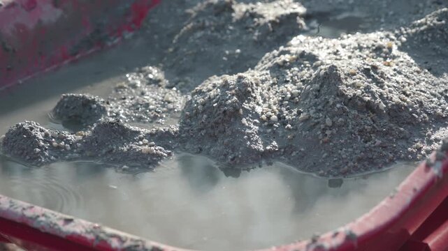 detailed close-up of wet grey cement mixed with sand and water inside a red wheelbarrow.