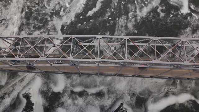 Editorial-style aerial footage capturing winter bridge traffic in Dubuque, Iowa. Frozen river conditions and steady vehicle movement show daily life and transportation infrastructure in cold weather.